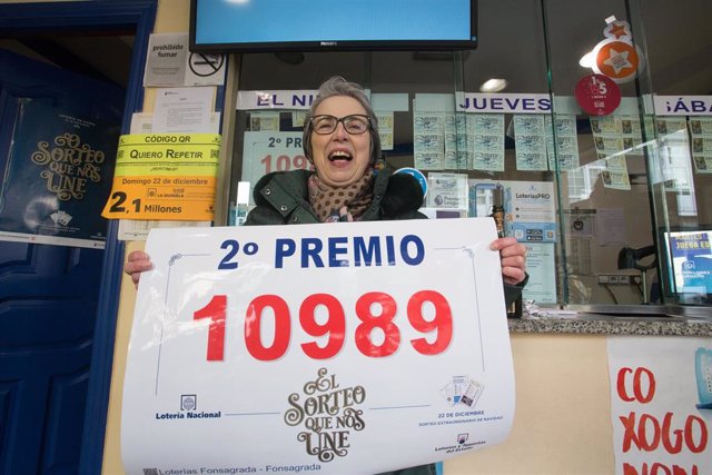 La propietaria de la administración de lotería nº1 de Fonsagrada,Otilia, posa con el número 10989, premiado con el Segundo Premio del Sorteo Extraordinario de Lotería de Navidad 2019, en Fonsagrada / Lugo /Galicia (España), a 22 de diciembre de 2019.
