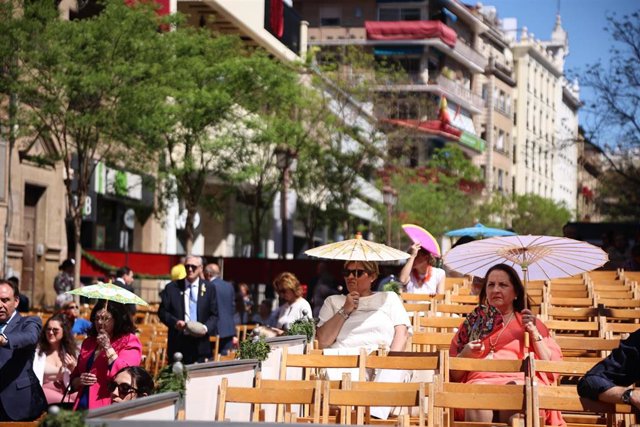 Las personas se protegen del intenso sol en las sillas de la Campana en Sevilla esperando la llegada de las cofradías