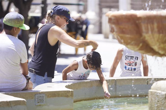 Archivo - Una madre le echa agua a su hijo, por la cabeza, en la fuente de la plaza Virgen de los Reyes en el primer día de la segunda ola de calor, a 7 de julio de 2022 en Sevilla (Andalucía, España)