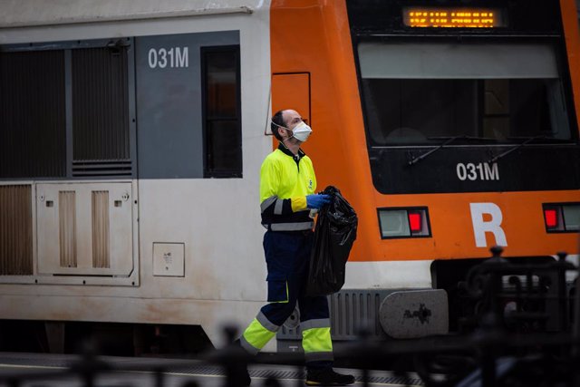 Archivo - Un treballador de la neteja al costat d'un tren de Rodalies