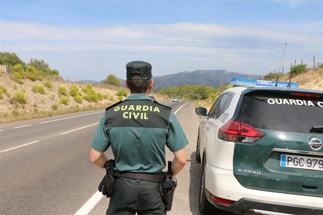 Archivo - Un agente de la Guardia Civil, junto a un vehículo del cuerpo.