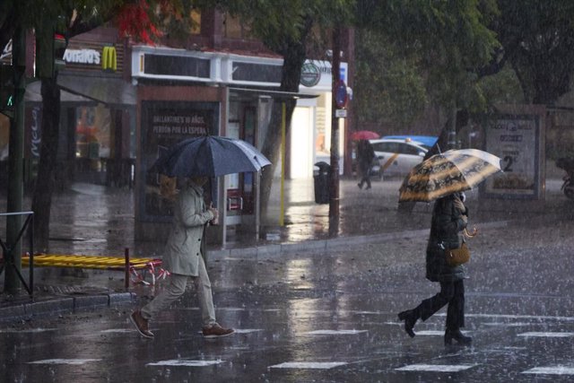 Archivo - Dos mujeres se refugian de la lluvia en sus paraguas 