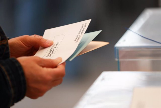 Una persona sostiene papeletas electorales frente a las urnas