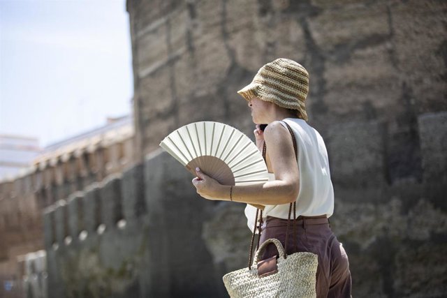 Una mujer se protege del sol con sombrero y abanico. Imagen de archivo.
