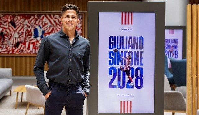 Giuliano Simeone posando junto a un cartel que anuncia su renovación con el Atlético hasta 2028.