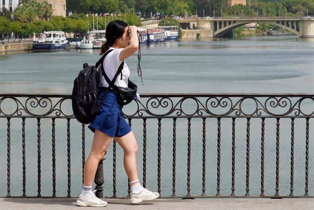 Una persona paseando por el Puente de Triana se protege la cara el día en que la capital está en alerta naranja por el calor , a 19 de julio del 2023. 