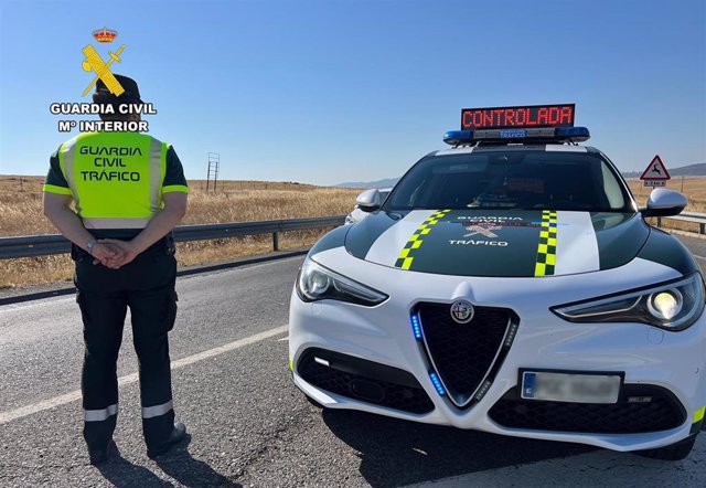 Archivo - Un agente de la Guardia Civil de Tráfico junto a su vehículo en una carretera.