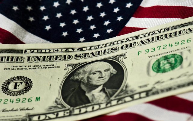 Archivo - Billete de dólar y bandera estadounidense.