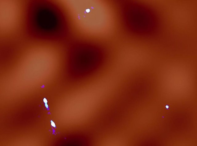 El color azul blanquecino representa las imágenes obtenidas con lentes gravitacionales observadas por ALMA. La distribución calculada de materia oscura se muestra en naranja; las regiones más brillantes indican concentraciones más altas de materia oscura