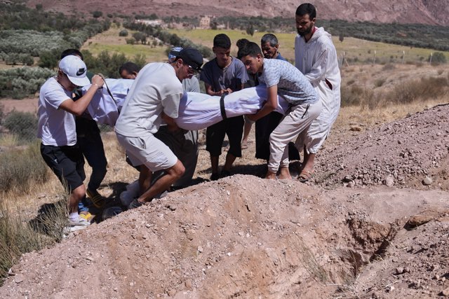 Varias personas llevan a enterrar a un hombre fallecido que ha sido rescatado de entre los escombros.