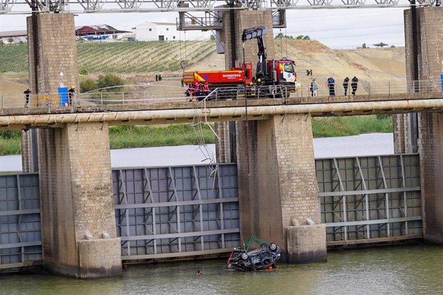 Momento en el que los bomberos logran sacar a la superficie el vehículo que se ha precipitado al río en Alcalá del Río y cuyo conductor ha fallecido.