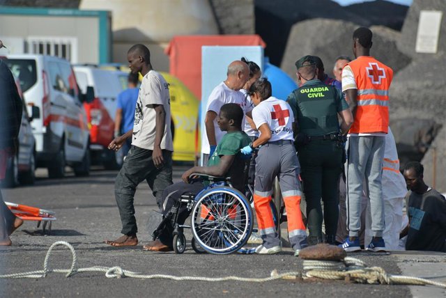Una trabajadora de la Cruz Roja traslada en silla de ruedas a uno de los migrantes llegados en un cayuco al puerto de La Restinga este lunes