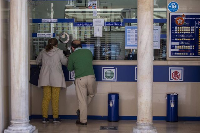 Archivo - Dos personas compran lotería en una Administración 