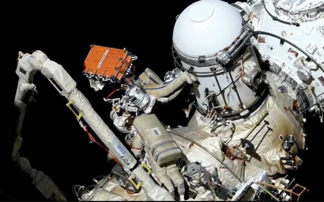 Los cosmonautas Oleg Kononenko (rayas rojas) y Nikolai Chub (rayas azules) preparan un sistema de comunicaciones por radar sintético para su instalación durante su caminata espacial de siete horas y 41 minutos.