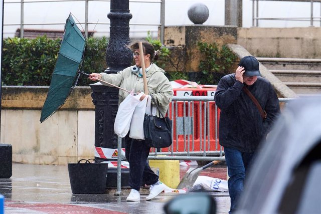 Varias personas tratan de cubrirse de la lluvia y el viento en Santander.