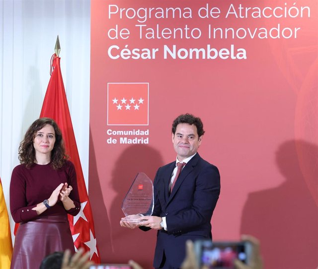 La presidenta de la Comunidad de Madrid, Isabel Díaz Ayuso, entrega un reconocimiento al hijo del investigador César Nombela, durante la presentación de las ayudas para la atracción del talento investigador de la Comunidad de Madrid.