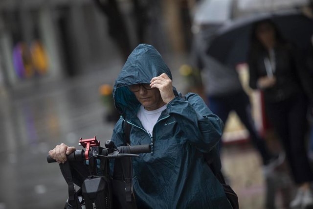 Archivo - Una mujer se coloca la capucha para protegerse de la lluvia. Imagen de archivo.