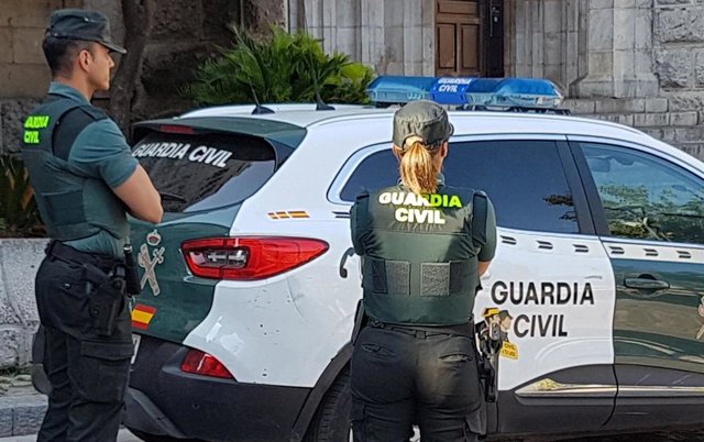 Archivo - Dos guardias civiles ante un vehículo de la Benemérita.