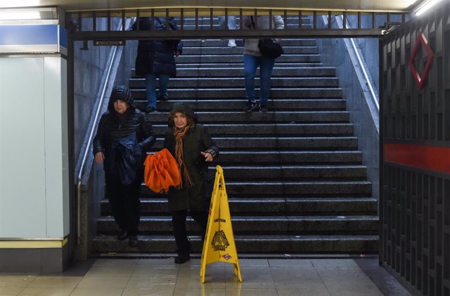 Archivo - Personas entran al metro con paraguas y mojadas por la lluvia