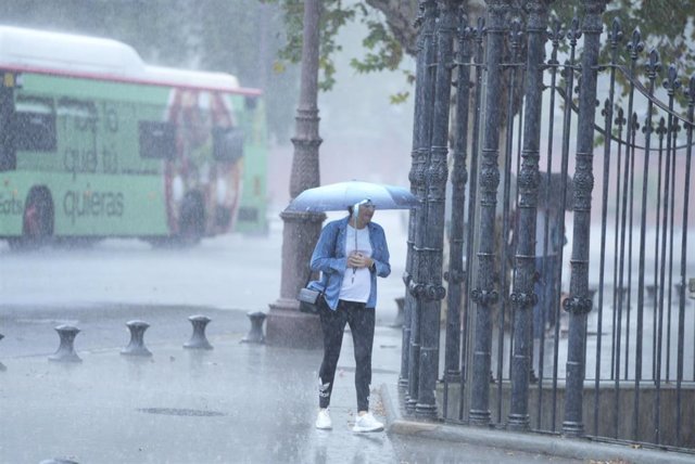 Archivo - Una persona camina bajo la lluvia por el centro de la ciudad.