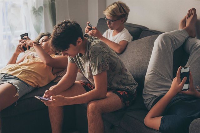 Archivo - Grupo de adolescentes sentados mirando sus móviles.