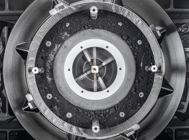 Una vista de arriba hacia abajo del cabezal del mecanismo de adquisición de muestras Touch-and-Go (TAGSAM) de OSIRIS-REx sin la tapa, que revela el resto de la muestra de asteroide en su interior.