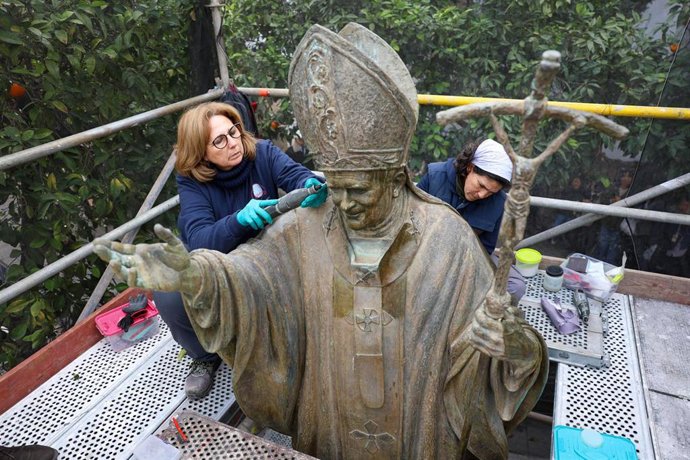 Dos mujeres acometen labores de limpieza en el monumento a Juan Pablo II de la Plaza Virgen de los Reyes.