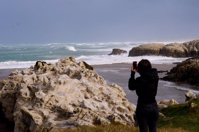 Archivo - Una persona fotografía las olas rompiendo en Santander