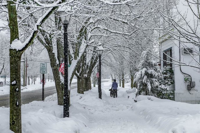 Archivo - US, Milford: A woman walks her dog on a snow-covered sidewalk amid heavy snowfall. 