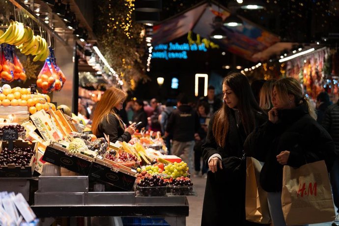 Archivo - Varias personas miran el género expuesto, en el Mercado de la Boquería