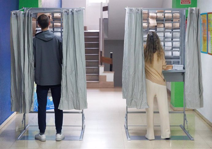 Archivo - Dos personas ejercen su derecho a voto en una cabina en un colegio electoral, a 28 de mayo de 2023, en Madrid (España).  